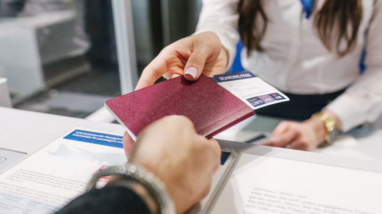 A close-up of a passport and boarding pass being handed to a female airport staff member as a man chicks in for his flight.