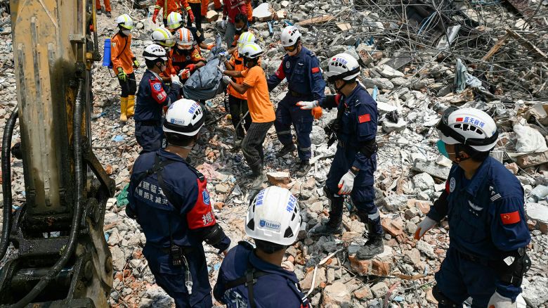 TOPSHOT - Myanmar and Chinese rescuers carry the body of a victim that was trapped under the rubble of the collapsed building 'Sky Villa Condominium development' in Mandalay on April 2, 2025, five days after a major earthquake struck central Myanmar. Days after a shallow 7.7-magnitude earthquake that killed more than 2,000 people, many people in Myanmar are still sleeping outdoors, either unable to return to ruined homes or afraid of further aftershocks. (Photo by Sai Aung MAIN / AFP) (Photo by SAI AUNG MAIN/AFP via Getty Images)          